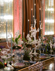 Elegant dining table setting with crystalware, candles, and floral arrangements in a luxurious room.