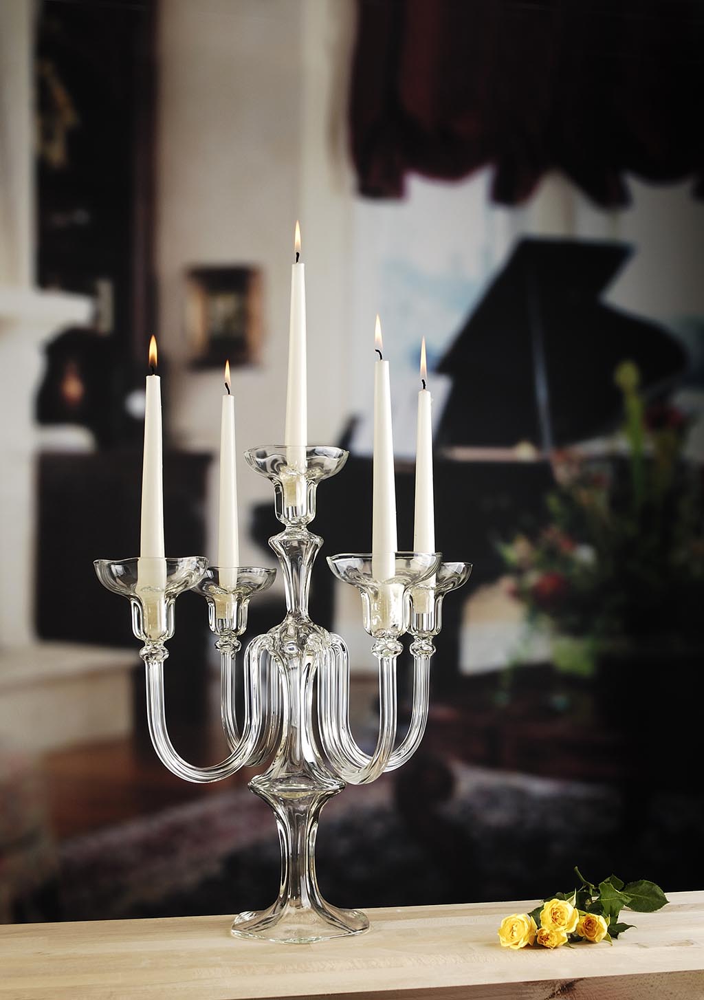 Clear glass candelabra with lit candles on a wooden surface, blurred background. Venus candelabra handmade in the Gabriela Seres Atelier