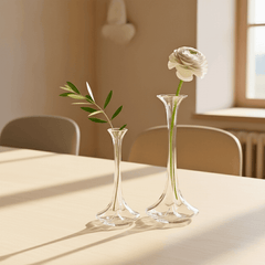 Two clear glass vases with a white rose and green leaves on a light surface.