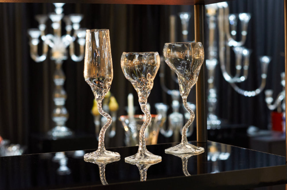 Three organic shaped glasses on a black shiny table and black sorrounding unfocused glass objects in the background.