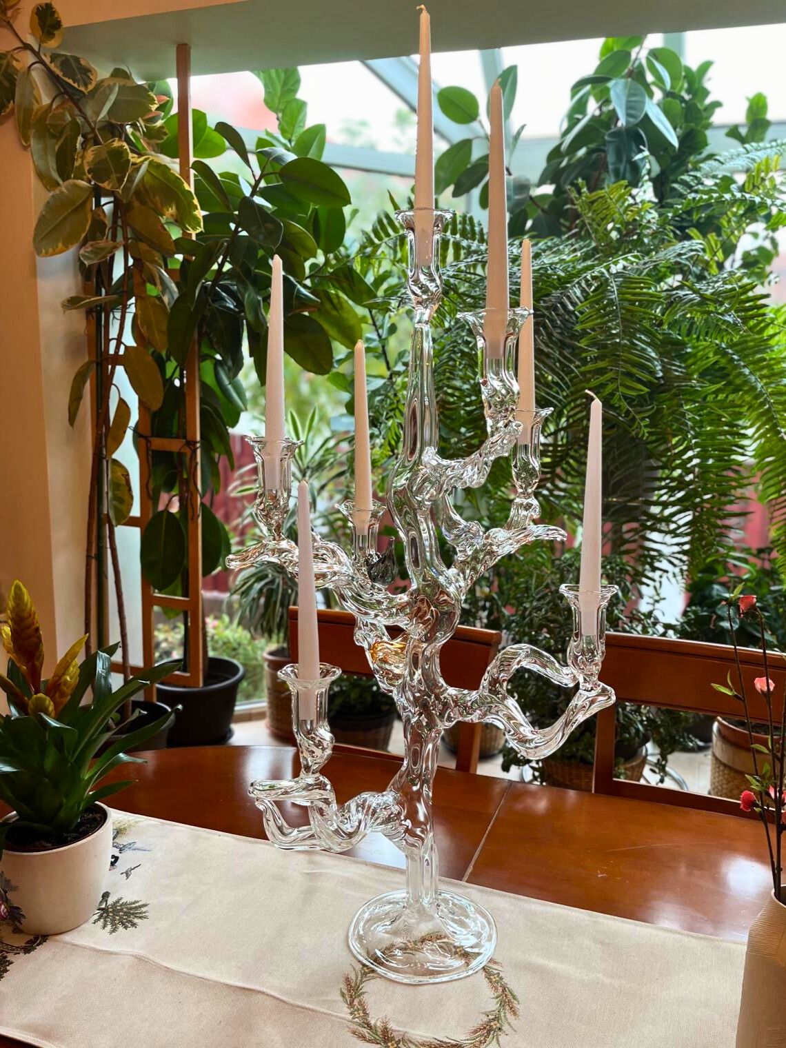 Clear glass candelabra with unlit candles on a table in a room with plants. Handmade in Bucharest at the Gabriela Seres atelier