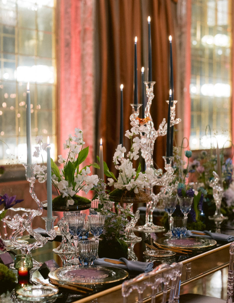 Elegant dining table setting with crystalware, candles, and floral arrangements in a luxurious room.