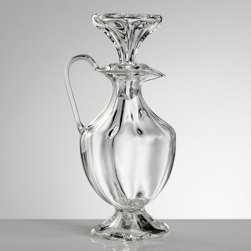 A clear glass oil bottle with a twisted metal top and a pouring spout, isolated on a white background.